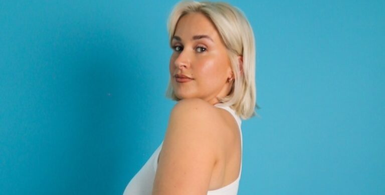 Photo of DJ Kennedy Taylor, a woman with short blonde hair, posing against a blue background