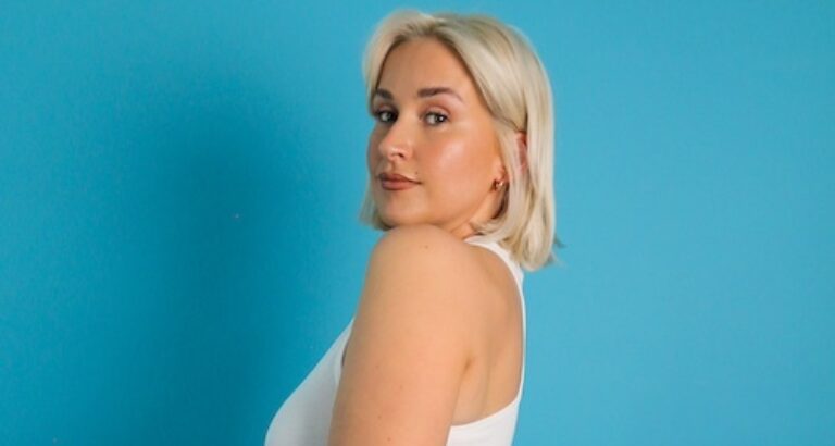Photo of DJ Kennedy Taylor, a woman with short blonde hair, posing against a blue background